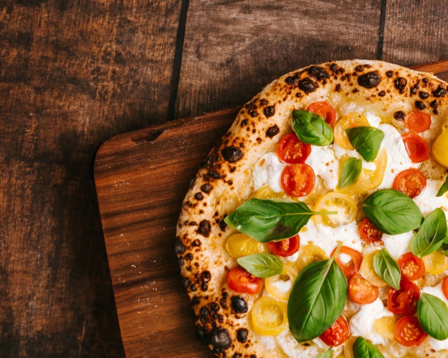 Frisch gebackene Pizza mit Mozzarella, bunten Kirschtomaten und Basilikum auf einem Holzbrett